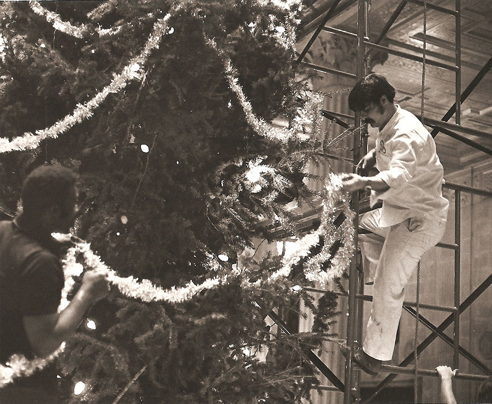 (FNB.2010.2.02) - Two Men Hang Garland on Christmas Tree in the Great Banking Hall, First National Center, c. 1974