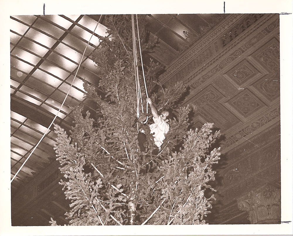 (FNB.2010.2.11) - Man Lifting Christmas Tree into Place, Great Banking Hall, First National Center, c. 1974